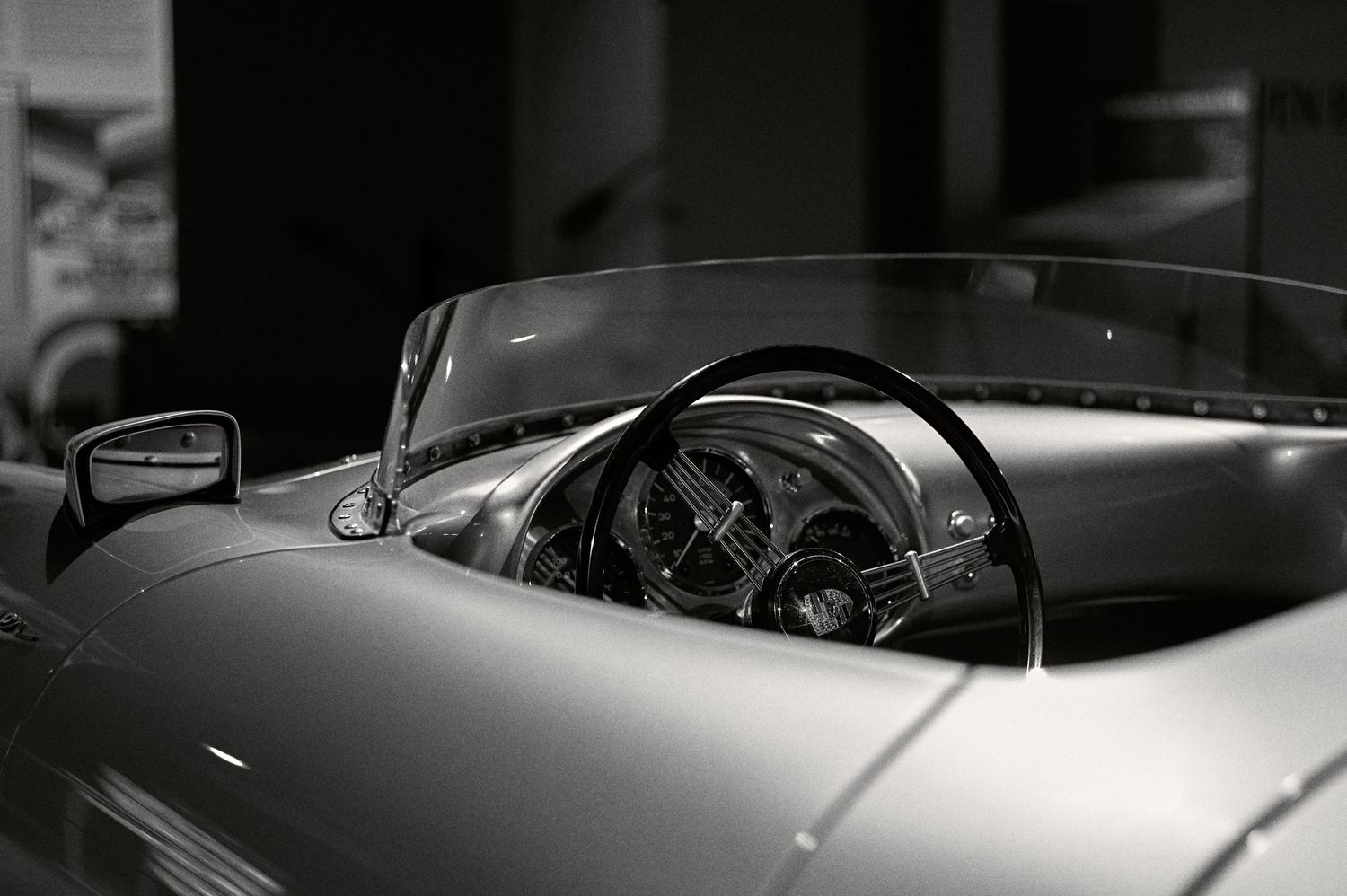 Black and white interior shot of a vintage sports car dashboard and steering wheel.