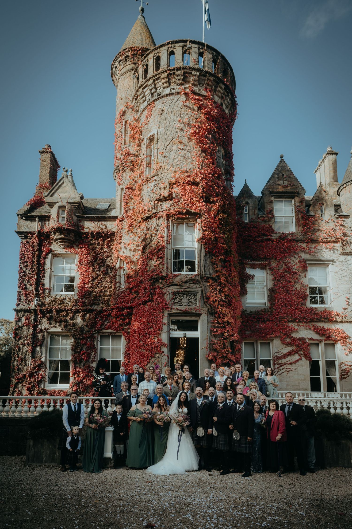Wedding party poses in front of a majestic Scottish castle covered in red autumn ivy.