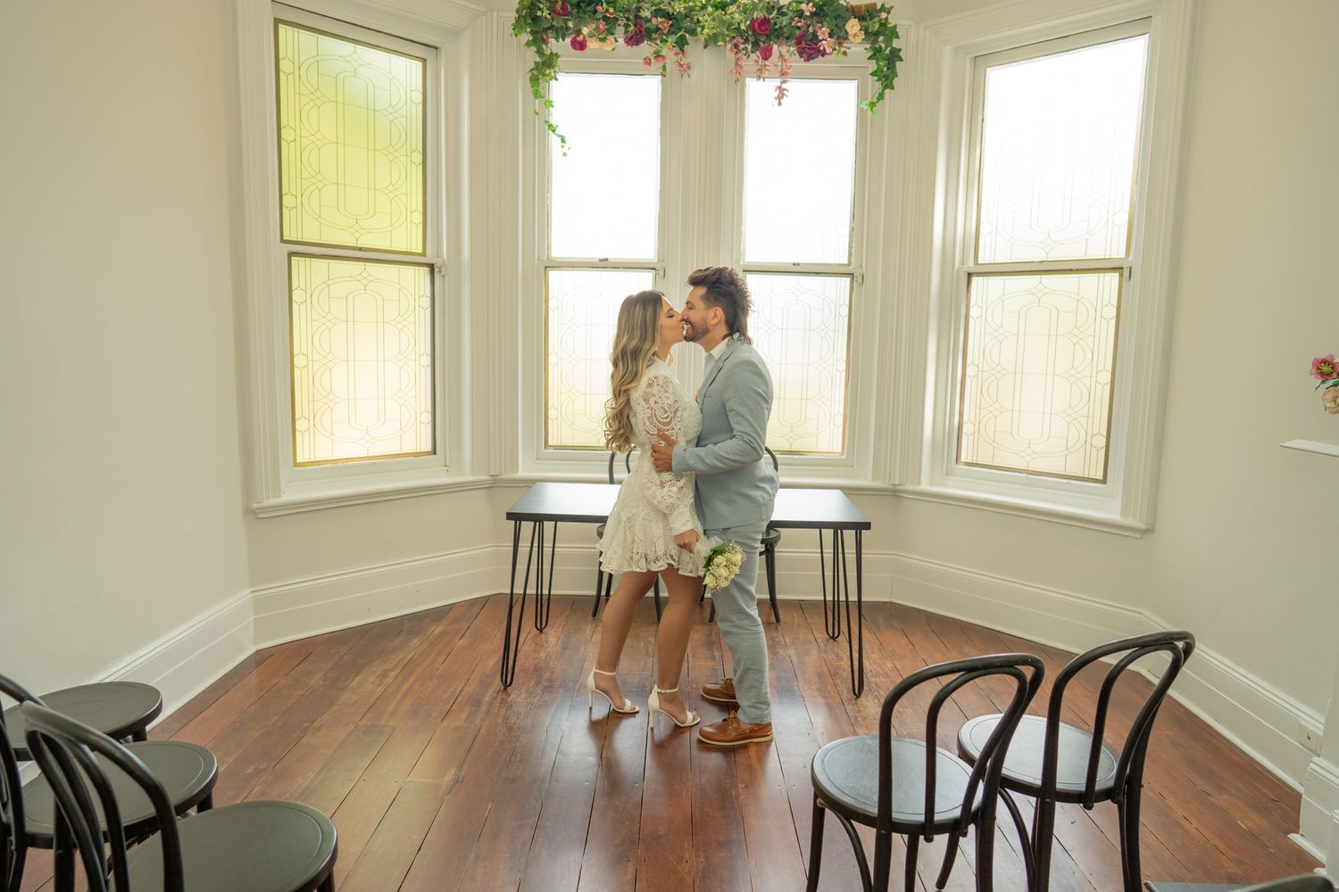 Private ceremony unfolds in minimalist room with hardwood floors and bay windows.
