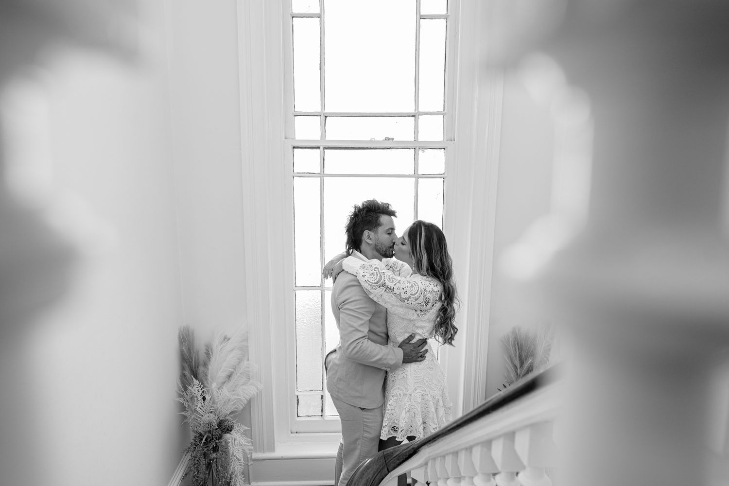 Black and white romantic moment captured on vintage staircase with natural window light.