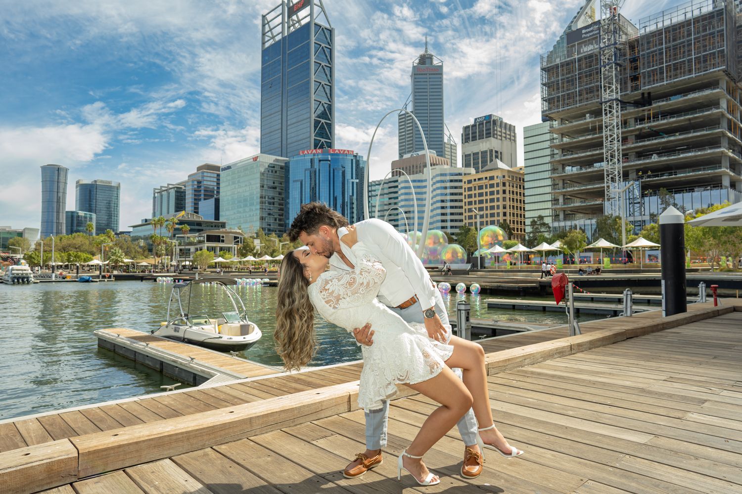A romantic dip pose on a wooden boardwalk with Perth's waterfront skyline in the background.