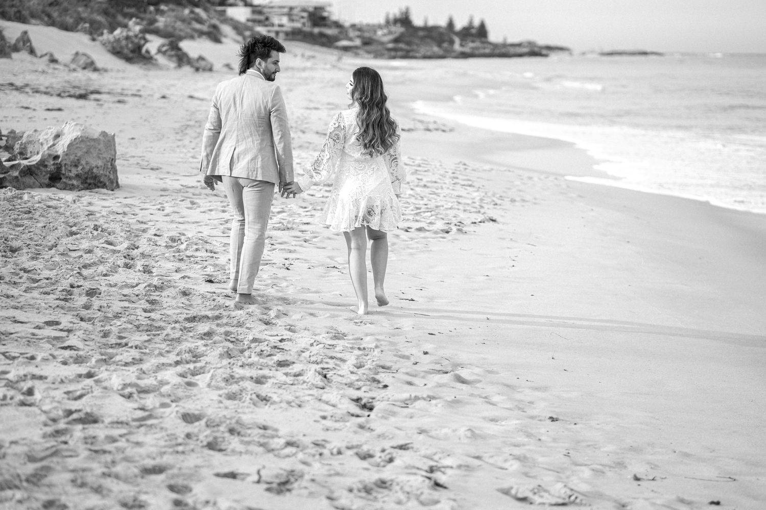 Black and white image of couple walking along peaceful shoreline.
