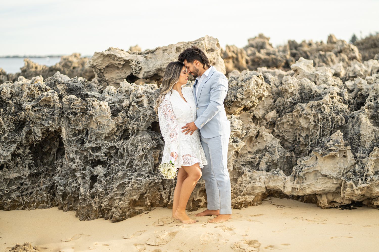Romantic moment captured against textured coastal rock formations at golden hour.