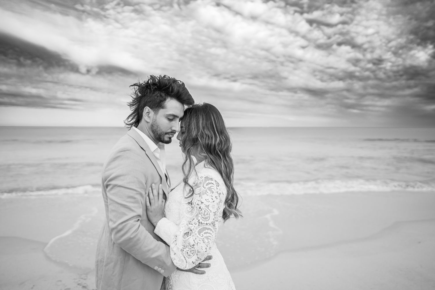 An intimate black and white portrait of a couple embracing on a windswept beach.