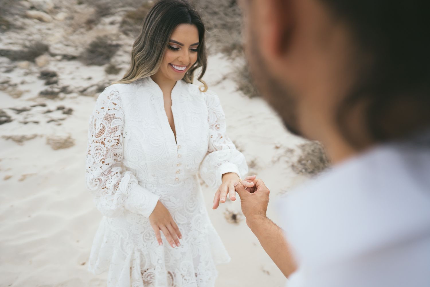 A proposal moment captured on a sandy beach with a white lace dress.