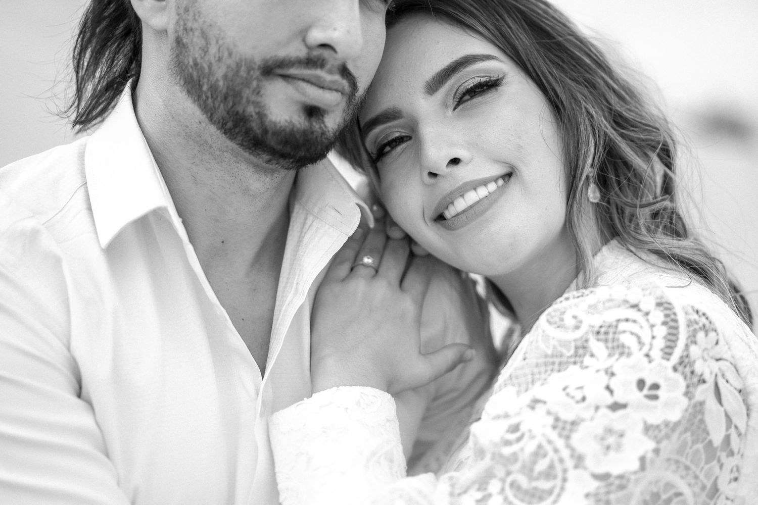A tender close-up portrait of a couple in white attire against a neutral background.