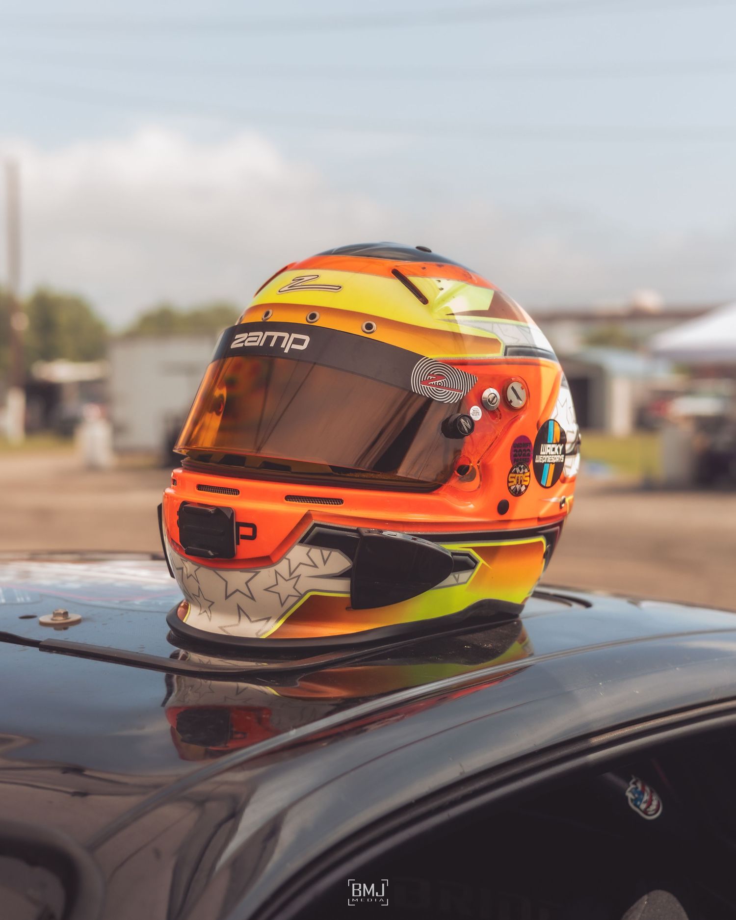 Colorful racecar helmet resting on hood of performance vehicle