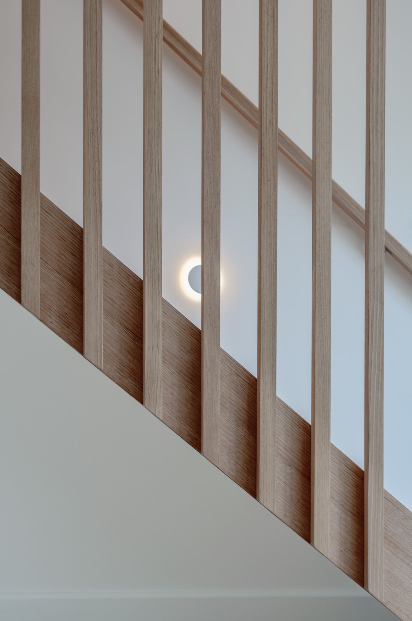 Modern wooden stair railing with white walls and built-in circular light fixture.