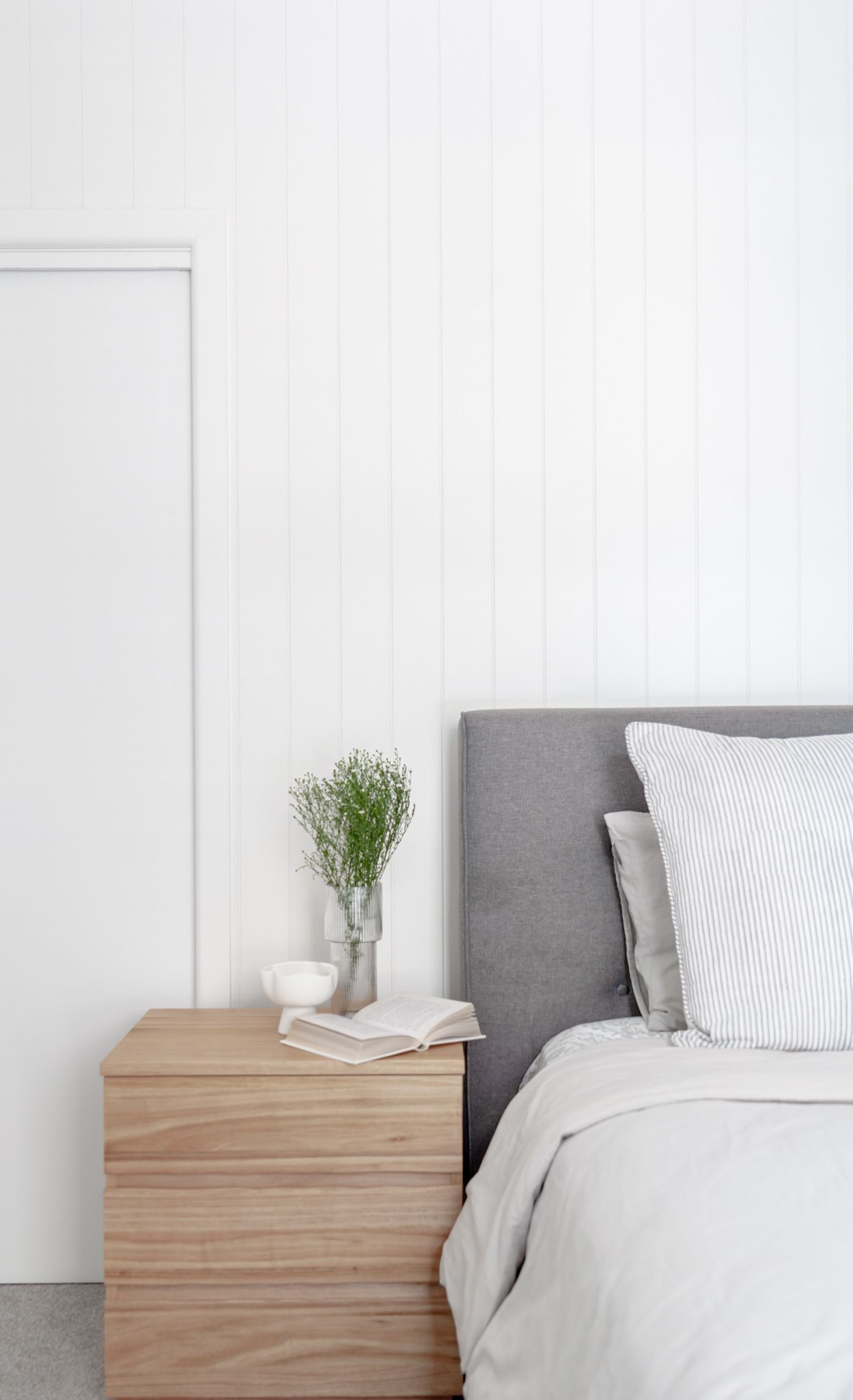 Scandinavian bedroom detail with wooden nightstand, gray headboard, and white bedding.
