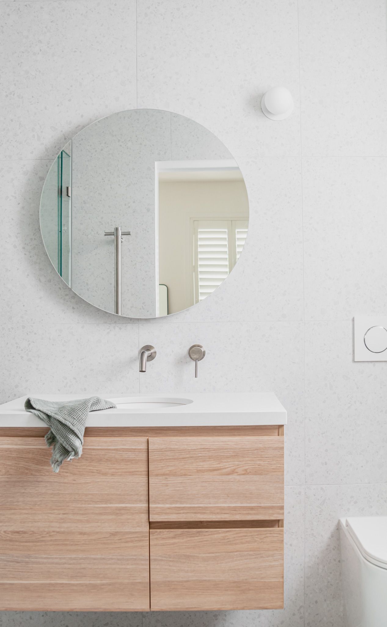 Contemporary bathroom vanity with round mirror, wall-mounted faucets, and light wood cabinetry.