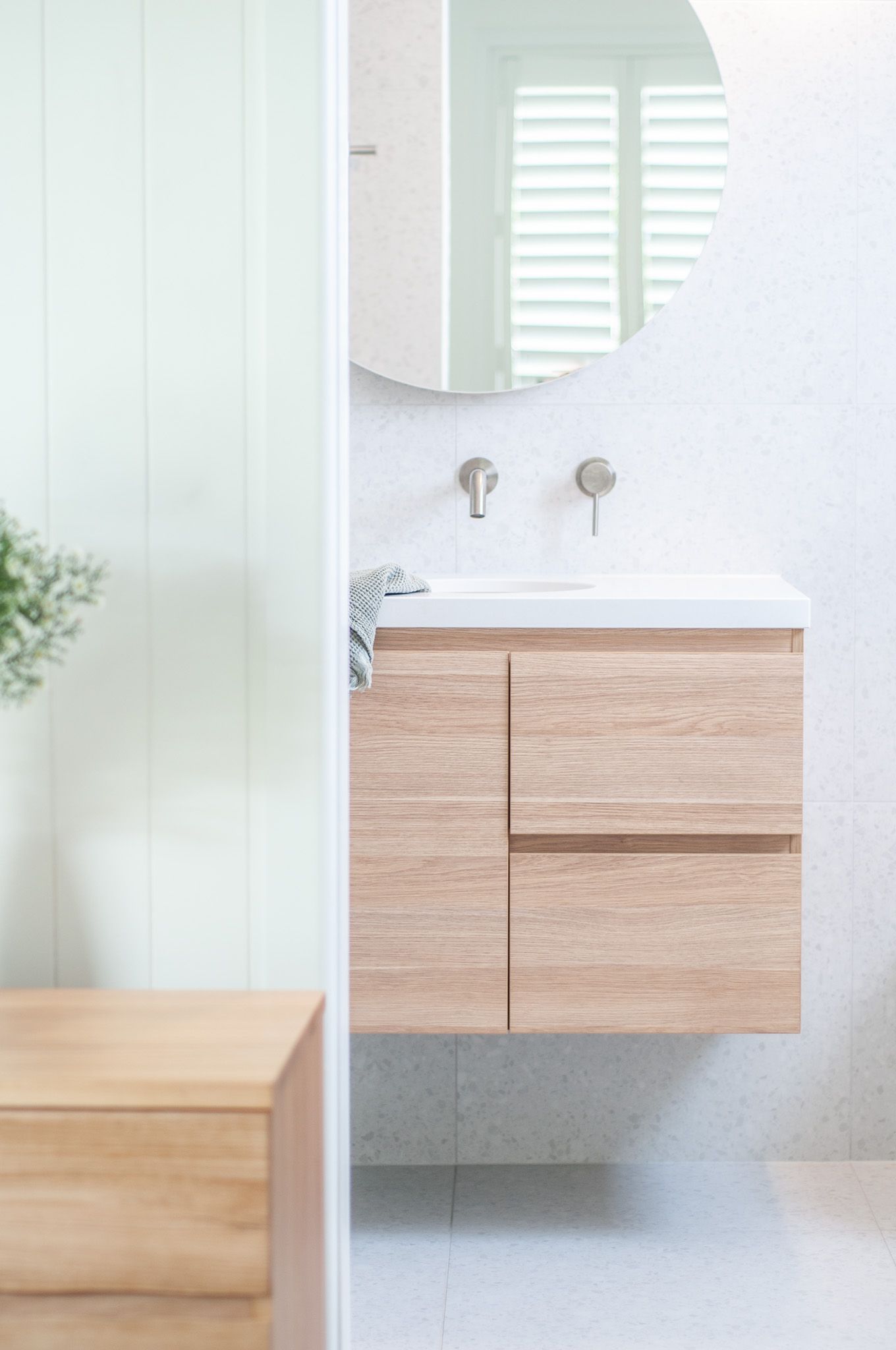 Minimalist bathroom interior with floating wood vanity, round mirror, and wall-mounted faucets.