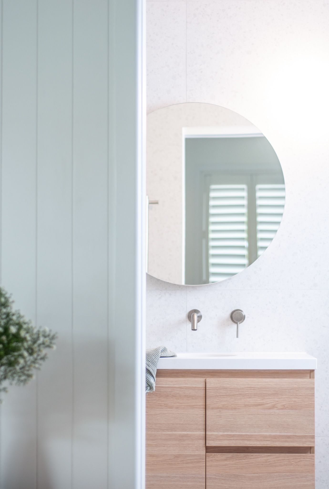 Clean bathroom design featuring round mirror, wood vanity and white vertical wall panels.