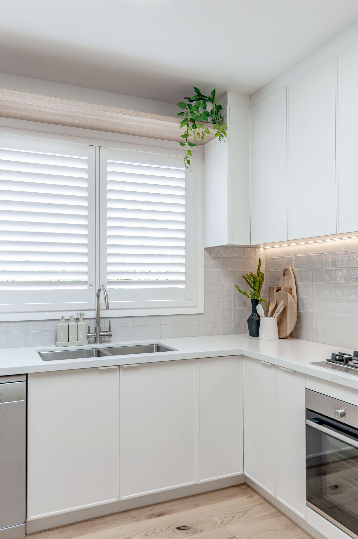 Bright L-shaped kitchen with white cabinetry, plantation shutters, and under-cabinet lighting.