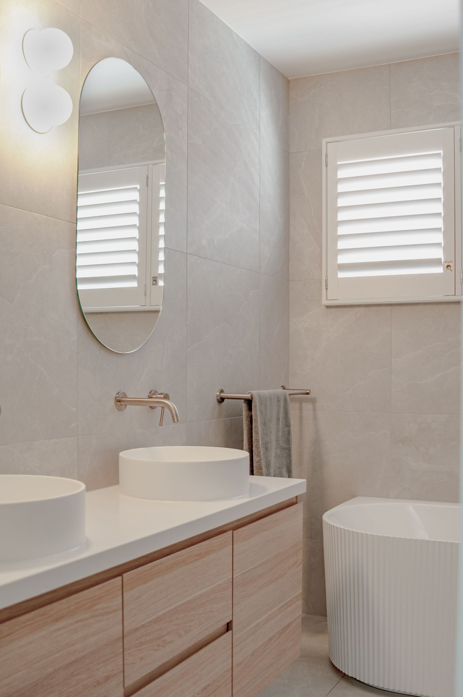 Contemporary bathroom featuring oval mirror, vessel sink, and plantation shutters with natural light.