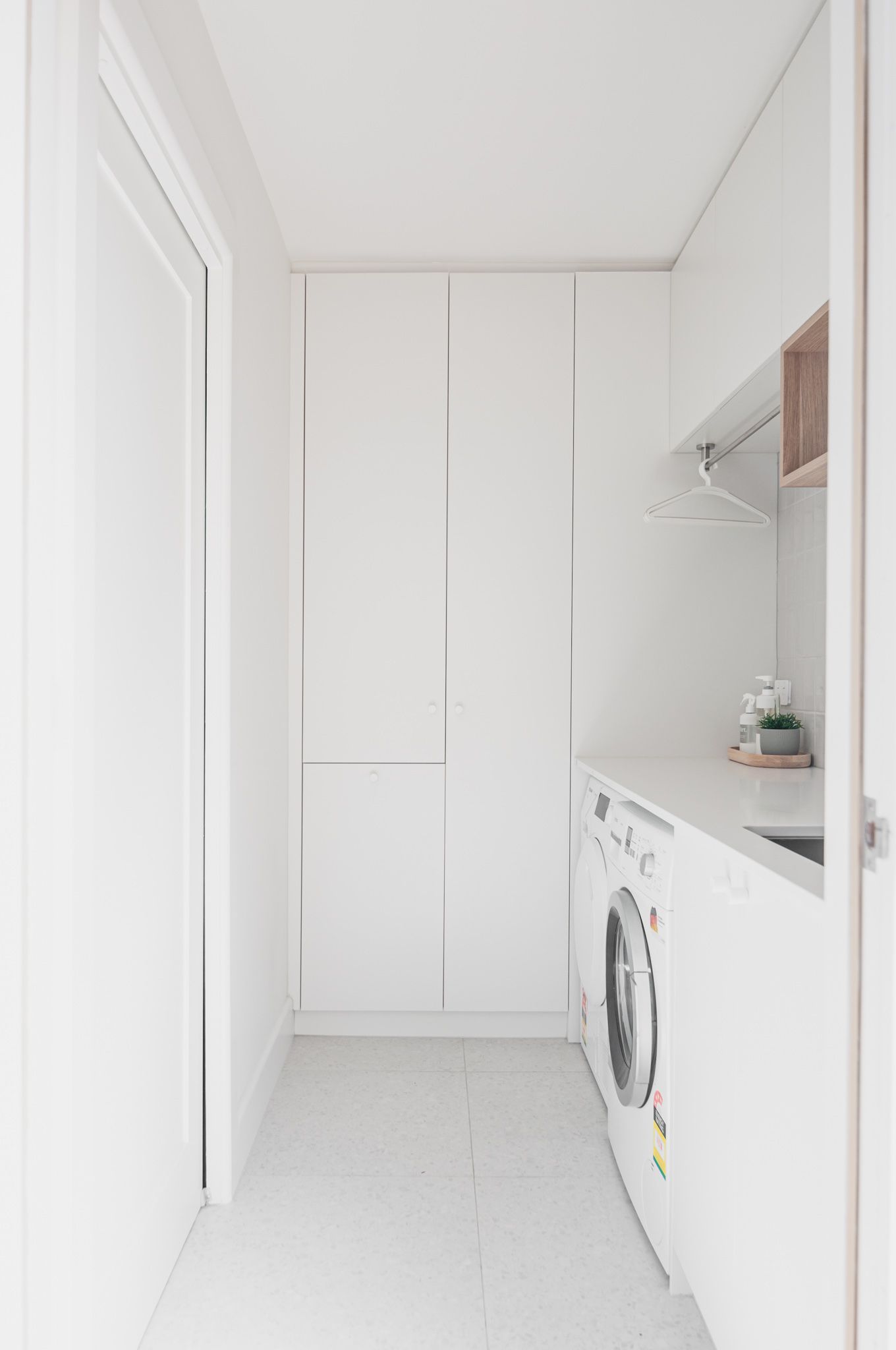 Clean white laundry room with built-in cabinets and front-loading washing machine.