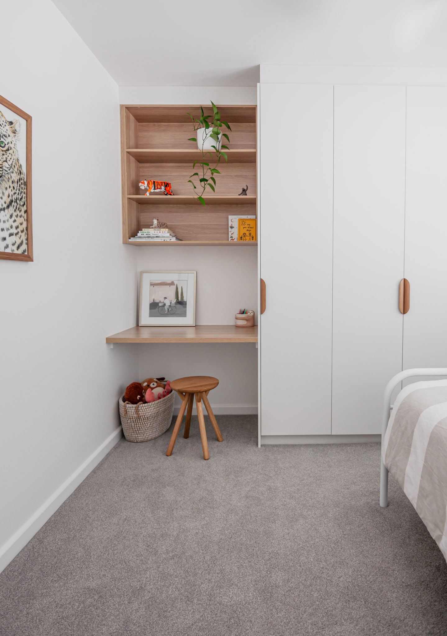Minimalist bedroom workspace with wooden shelving, white wardrobes, and a small wooden stool against gray carpet.