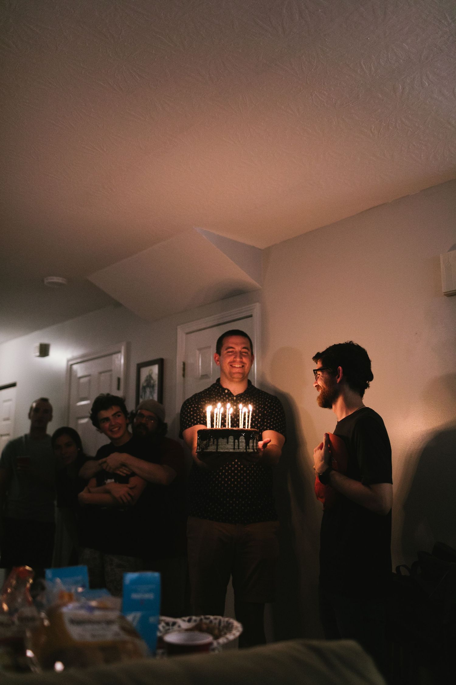Birthday celebration with lit candles on cake in dimly lit room.