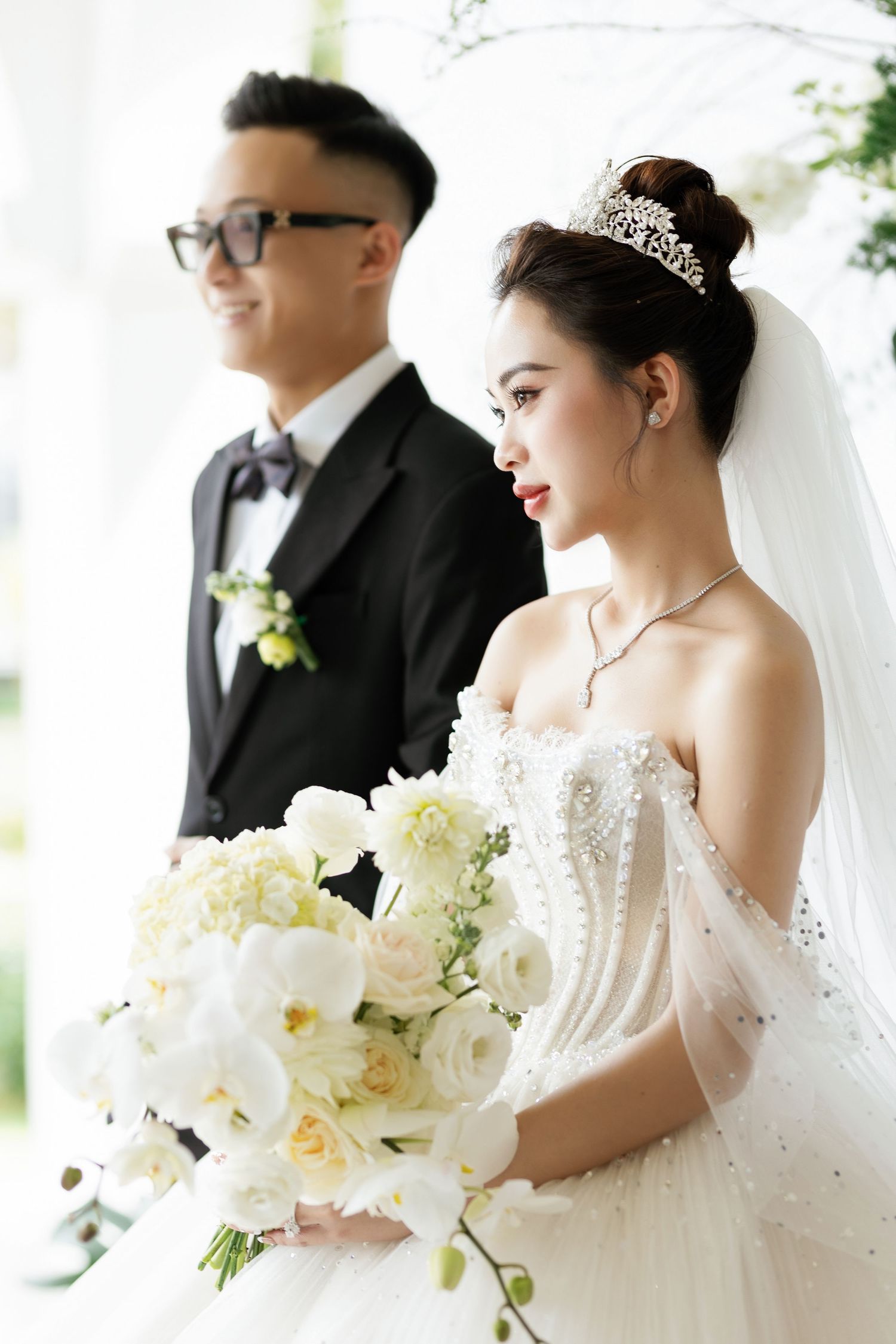 Elegant wedding portrait with bride in white gown holding bouquet next to groom in formal suit.