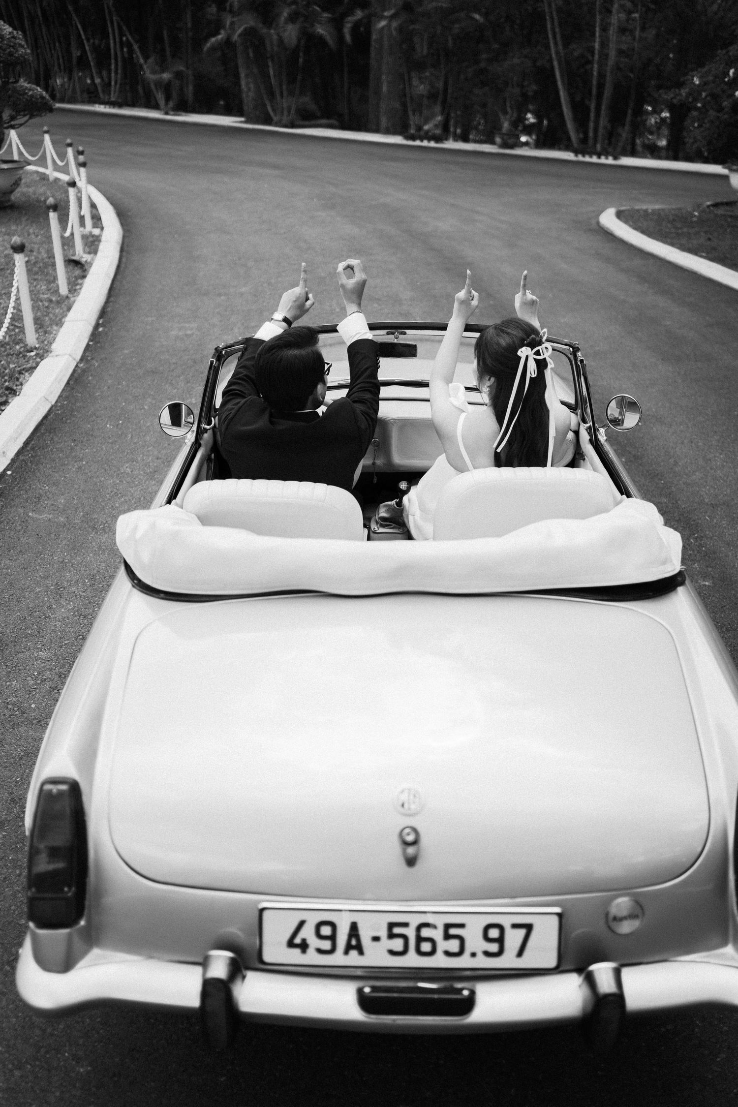 Vintage white convertible car on a curved road with raised hands visible from the back.
