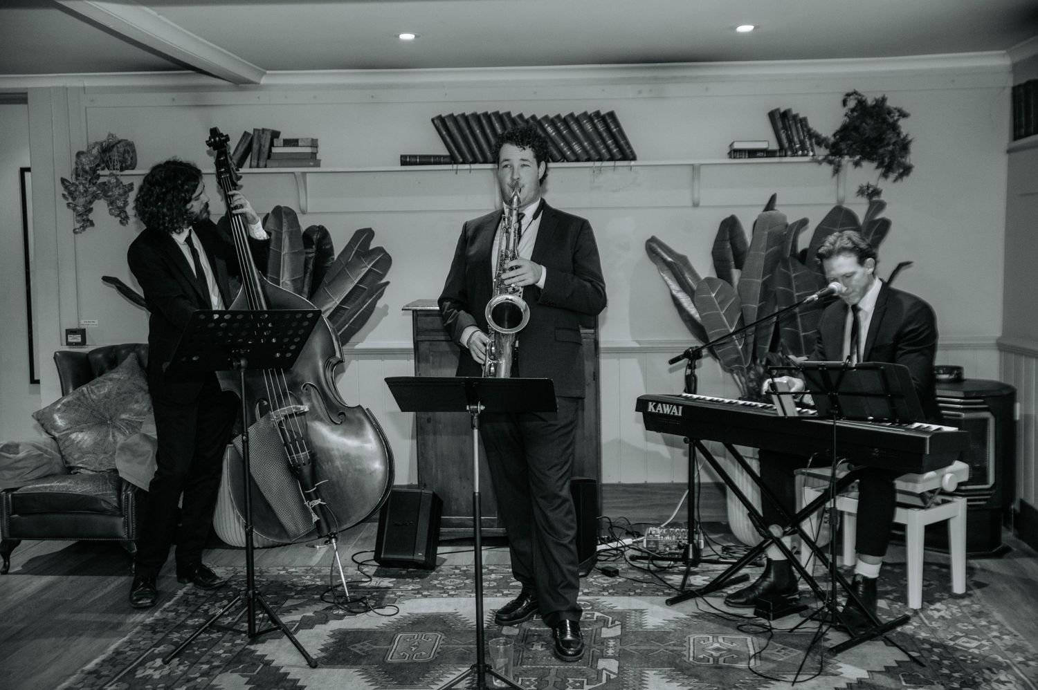 Black and white photo of jazz band performing with saxophone, bass, and keyboard at wedding reception.