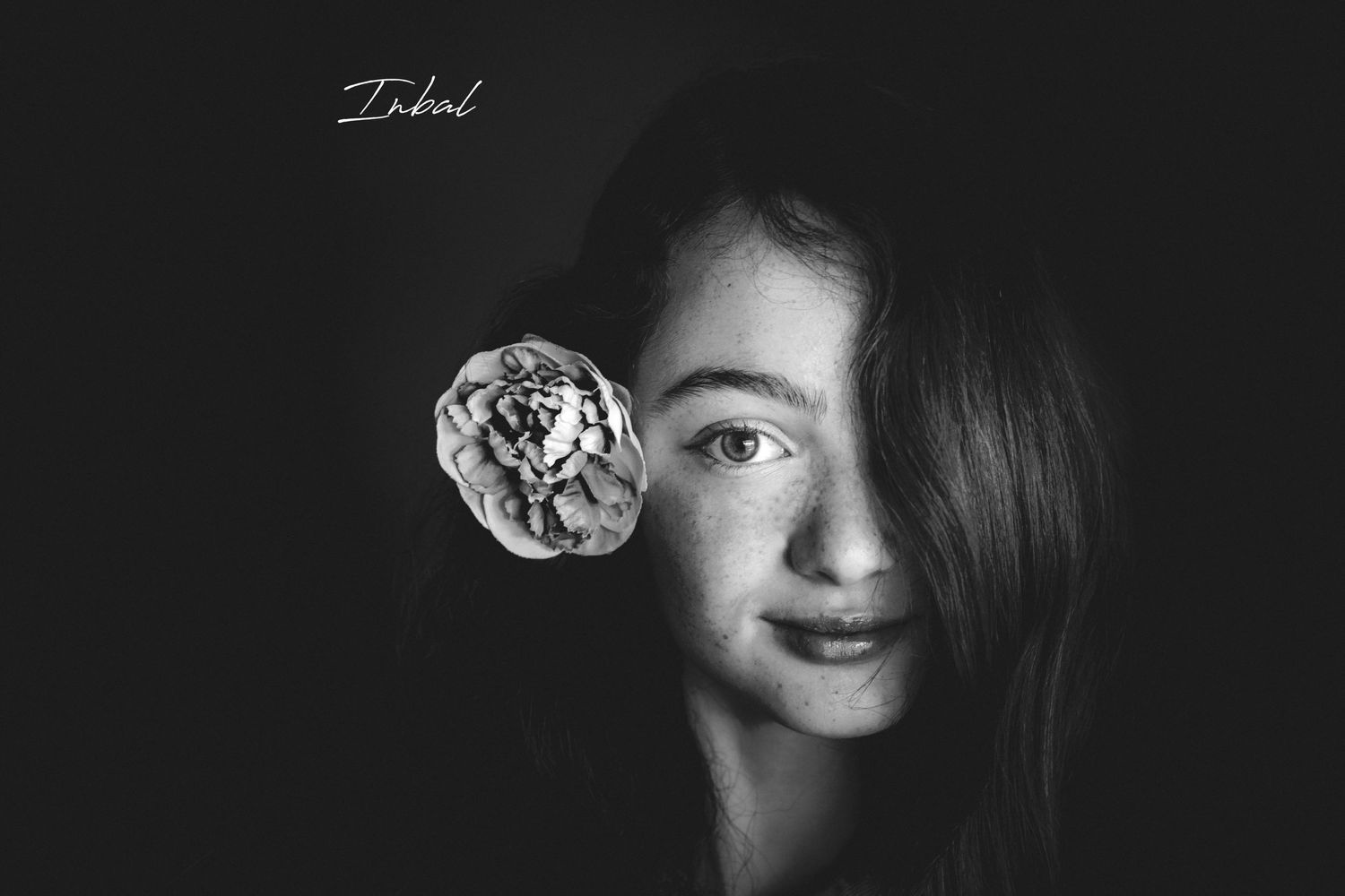 Black-and-white photo of a girl that her left side cover with her long curly hair and in the right ear she has a flower.