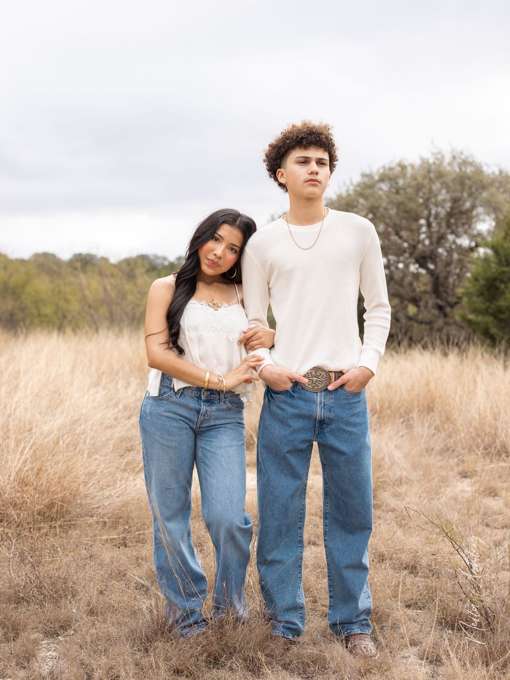 A couple wearing denim jeans poses together in a golden field during sunset.