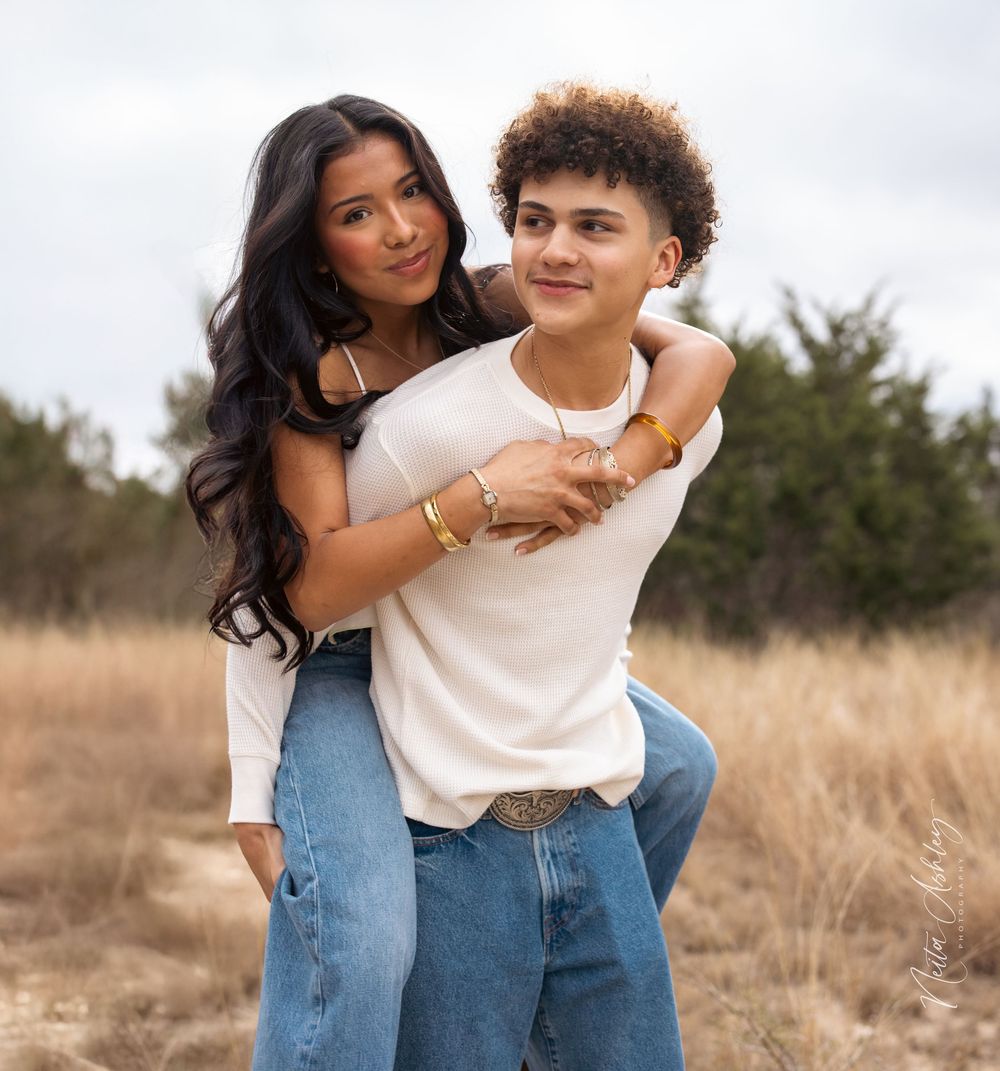 A couple shares playful piggyback moments together in a golden field during sunset.