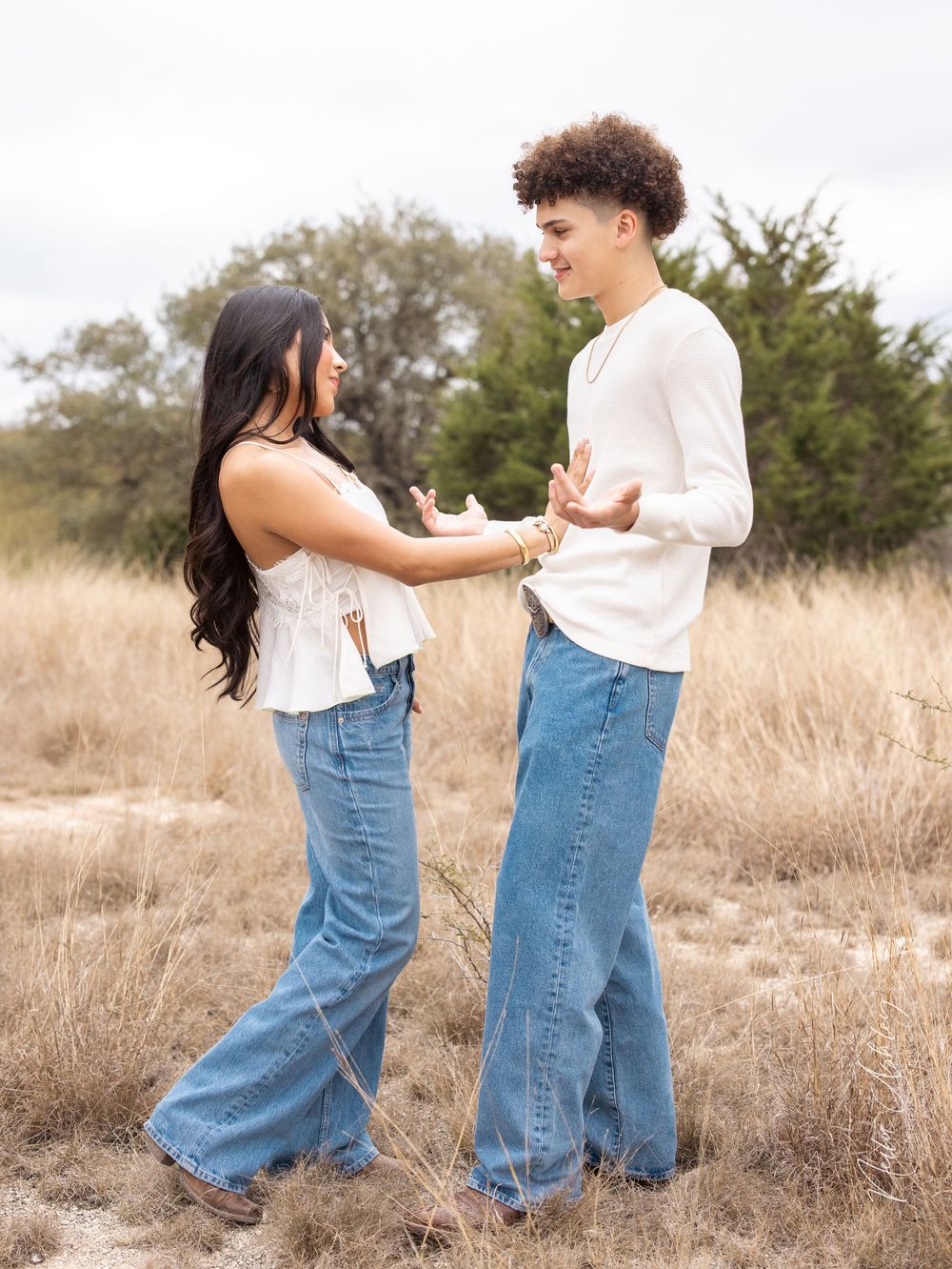 Young couple in casual white tops and blue jeans having an animated conversation in a field of dry grass.