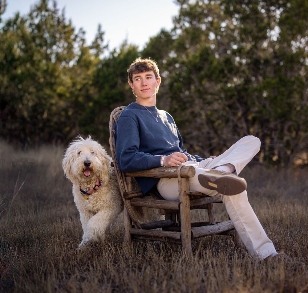 A young man relaxing on a wooden bench with a fluffy white dog in a rustic outdoor setting at dusk.