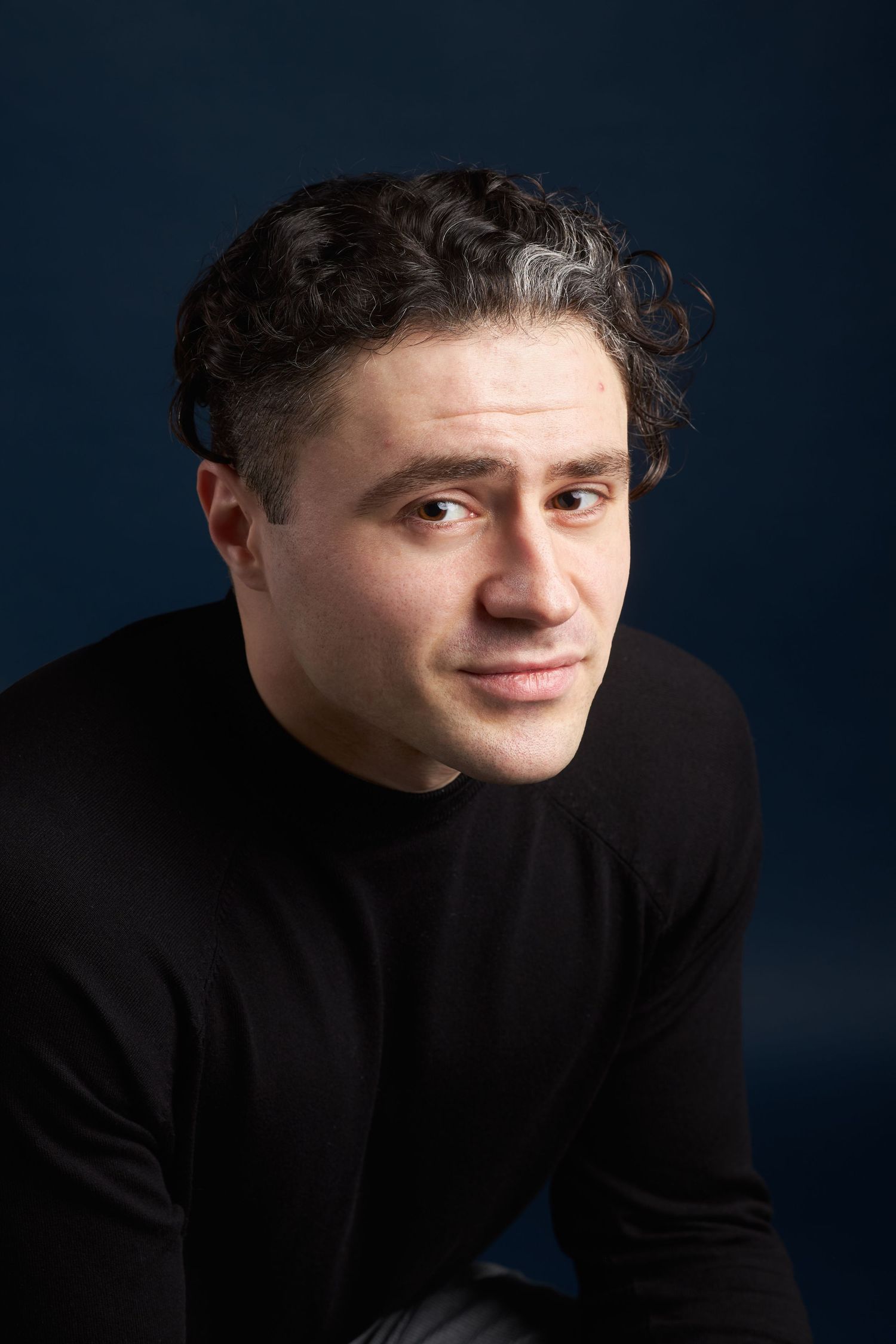 Professional studio portrait against dark blue background showing contemplative expression.