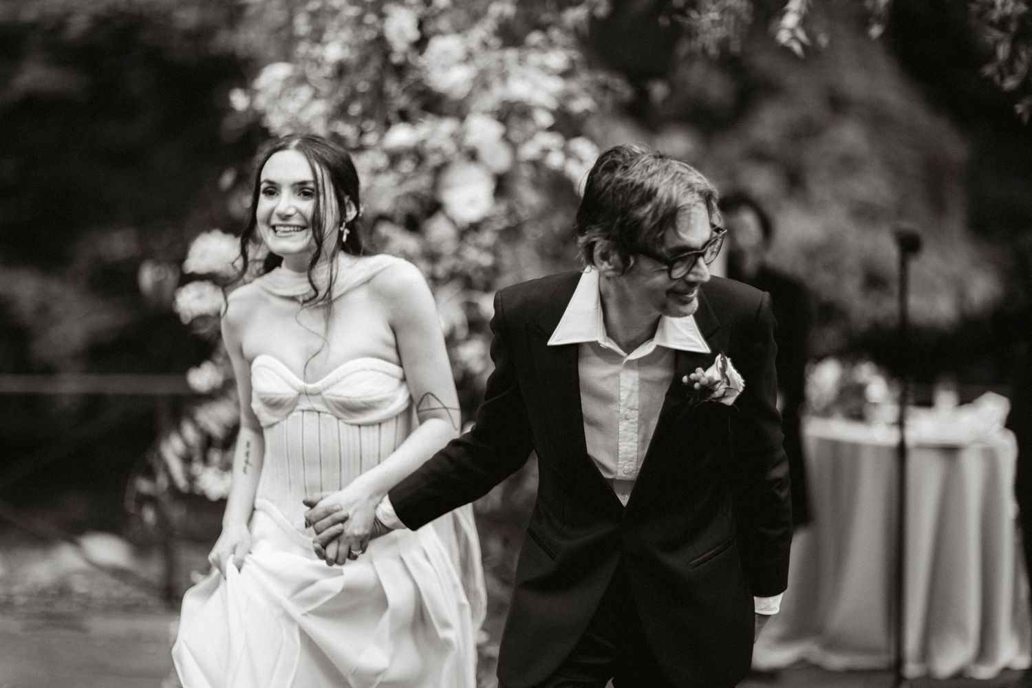 Black and white photo of newlyweds walking together and sharing a joyful moment.