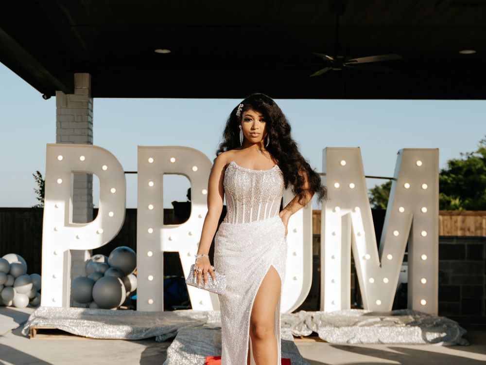 Elegant prom photo with illuminated PROM letter backdrop and formal white gown.