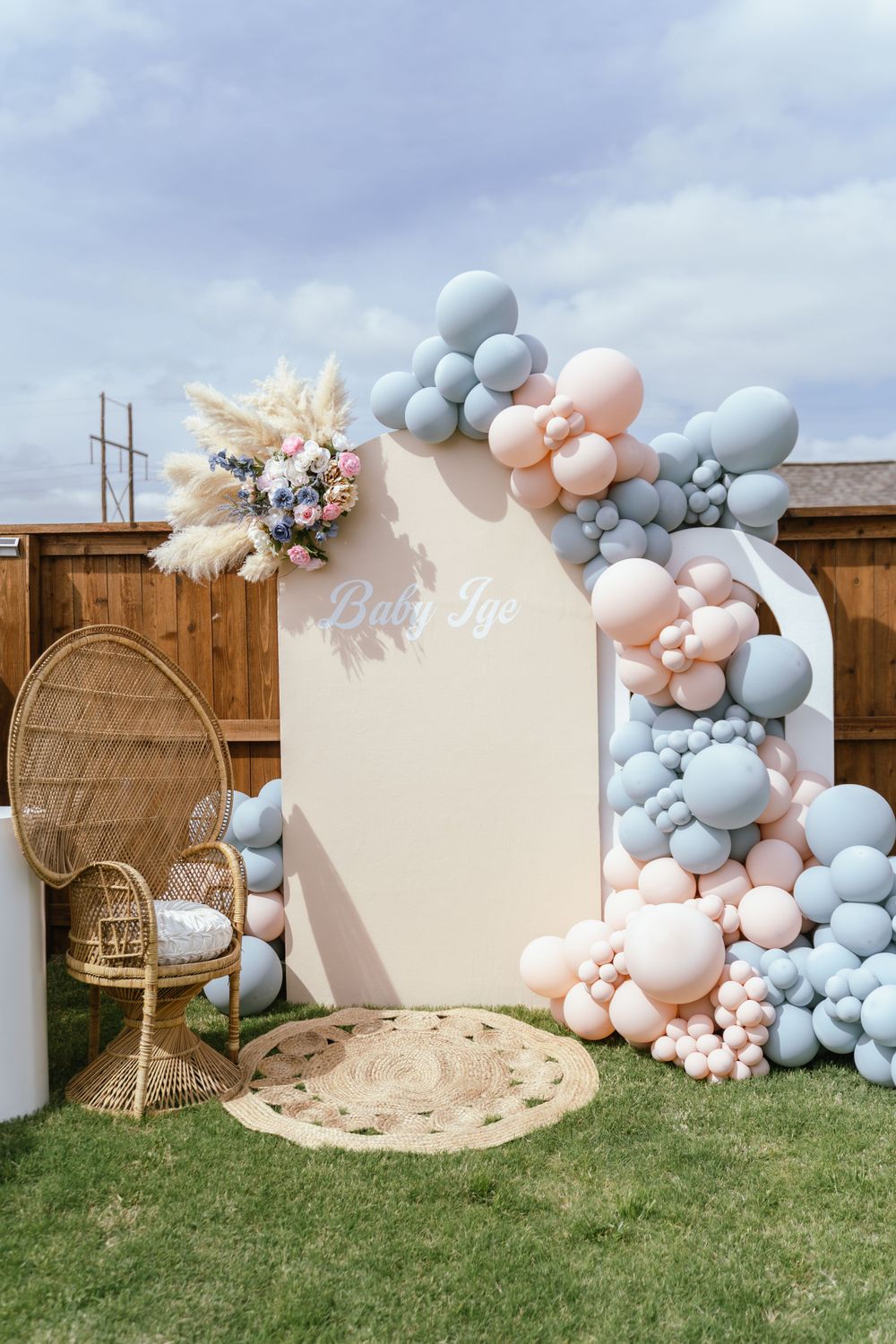 Elegant balloon arch installation with blush pink and grey balloons alongside a peacock chair and floral decor.