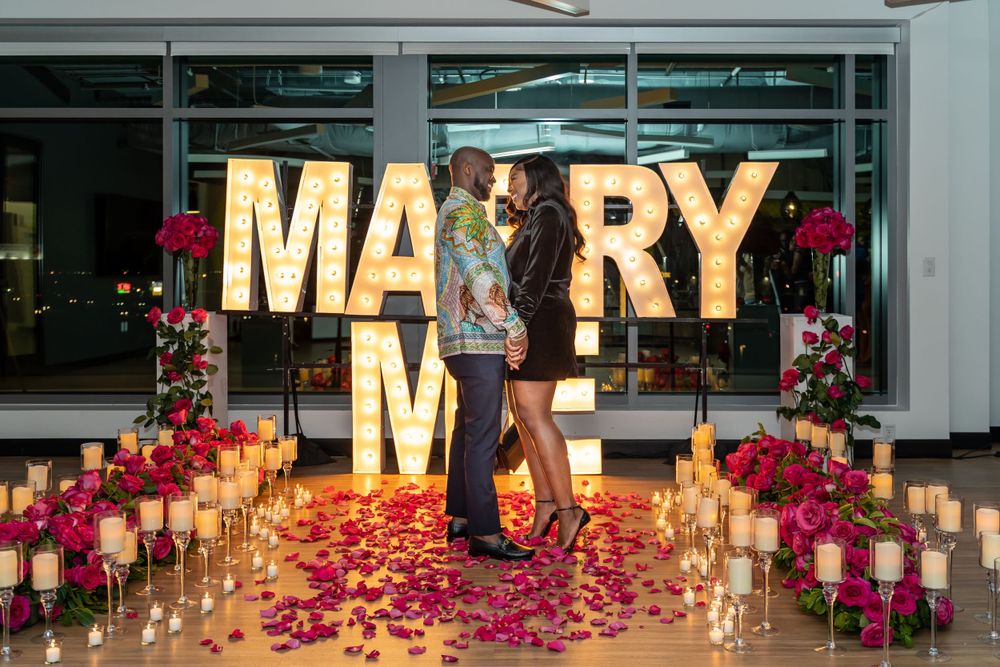 Romantic proposal setup with illuminated letters and candlelit path decorated with rose petals.