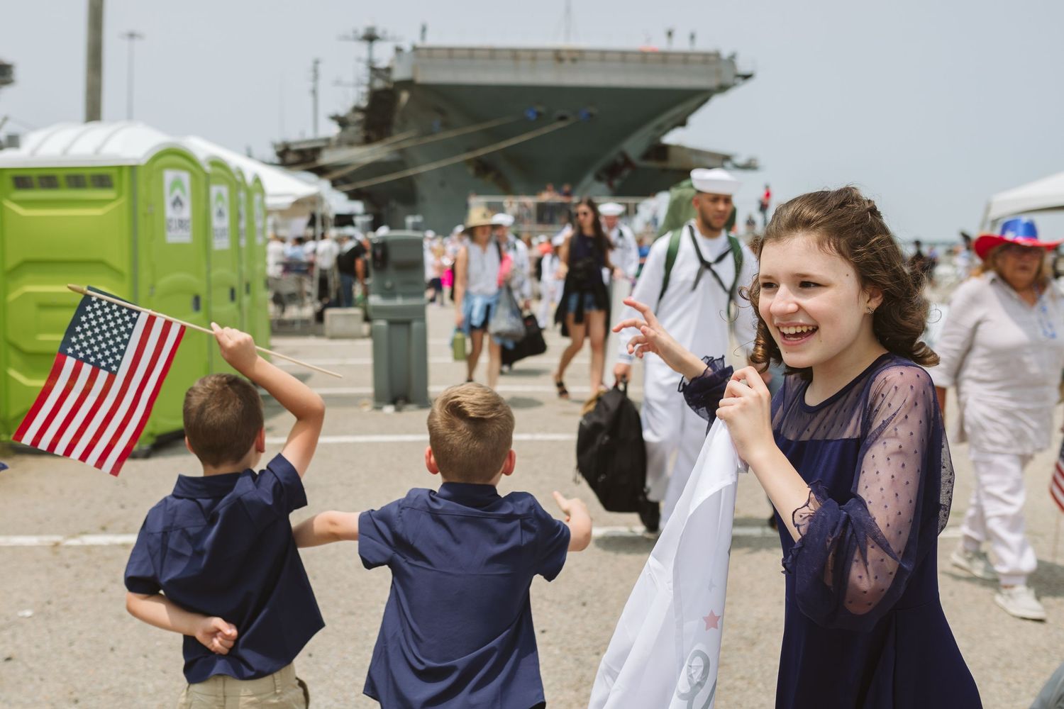 kids with flags and signs seeing dad for the first time with ship in the background in norfolk, virginia military homecoming
