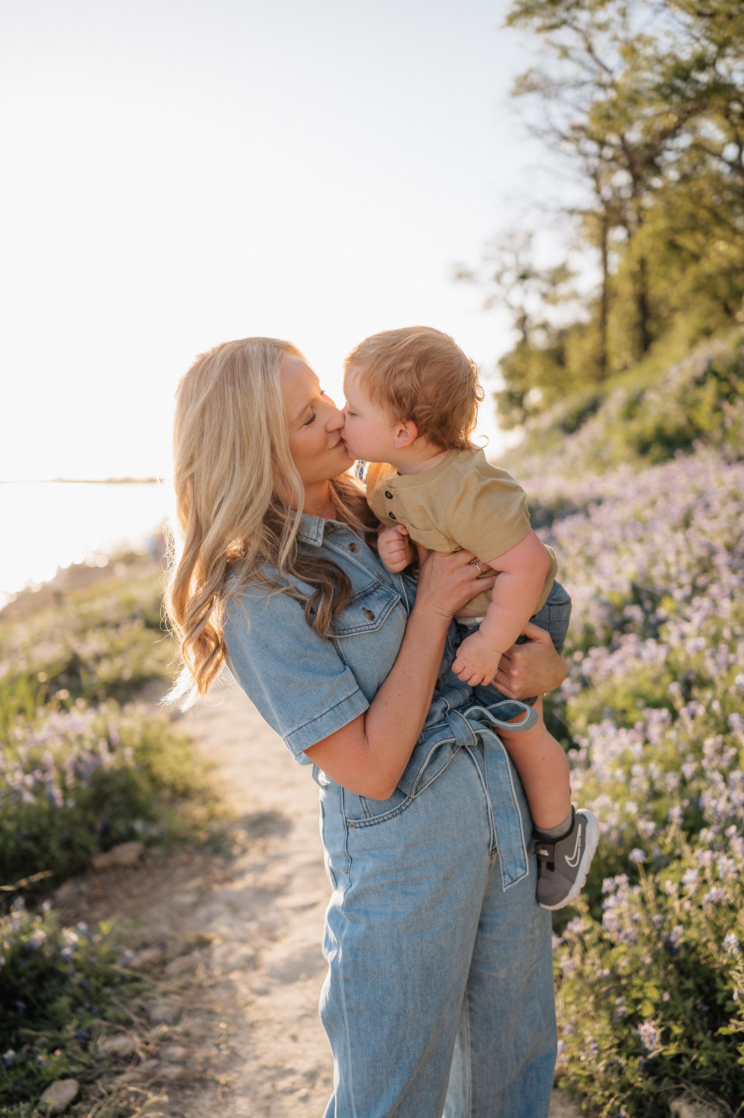 Parent and child share tender moment among wildflowers at sunset on coastal trail.