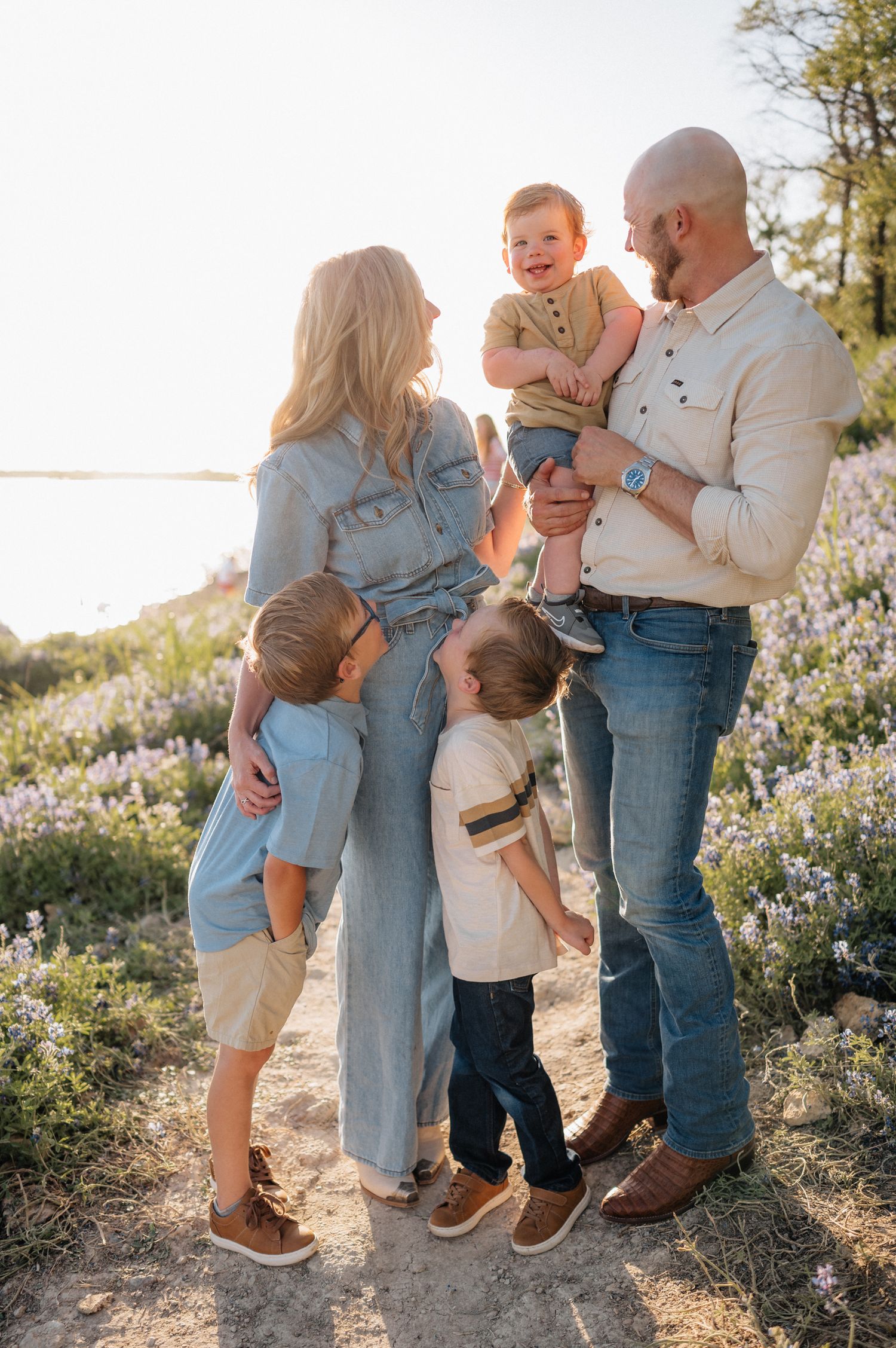 Family shares loving moment together on hillside path surrounded by spring wildflowers.
