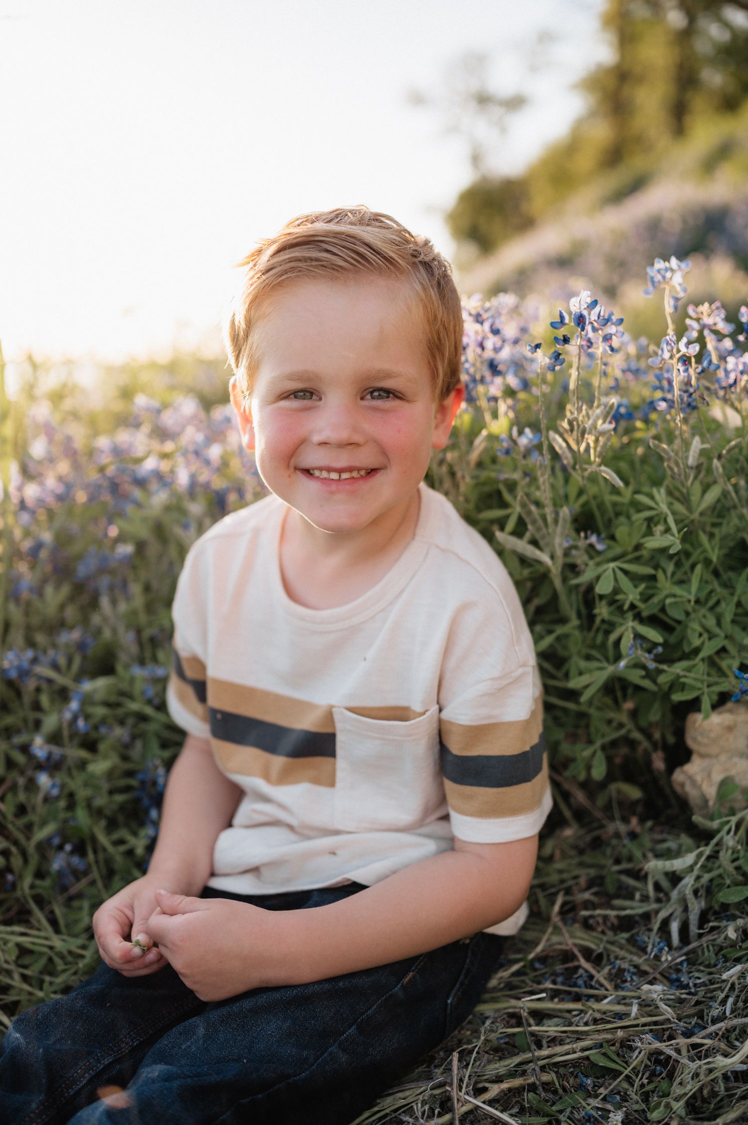 Young child sits smiling among purple wildflowers wearing striped t-shirt.