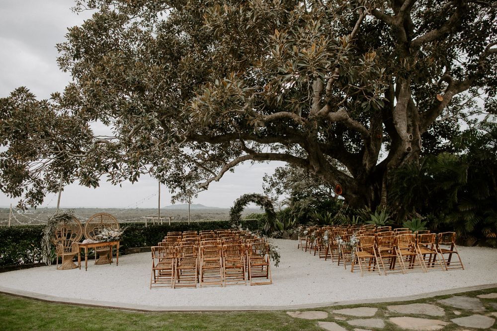 Outdoor wedding ceremony setup with wooden chairs under a large oak tree.