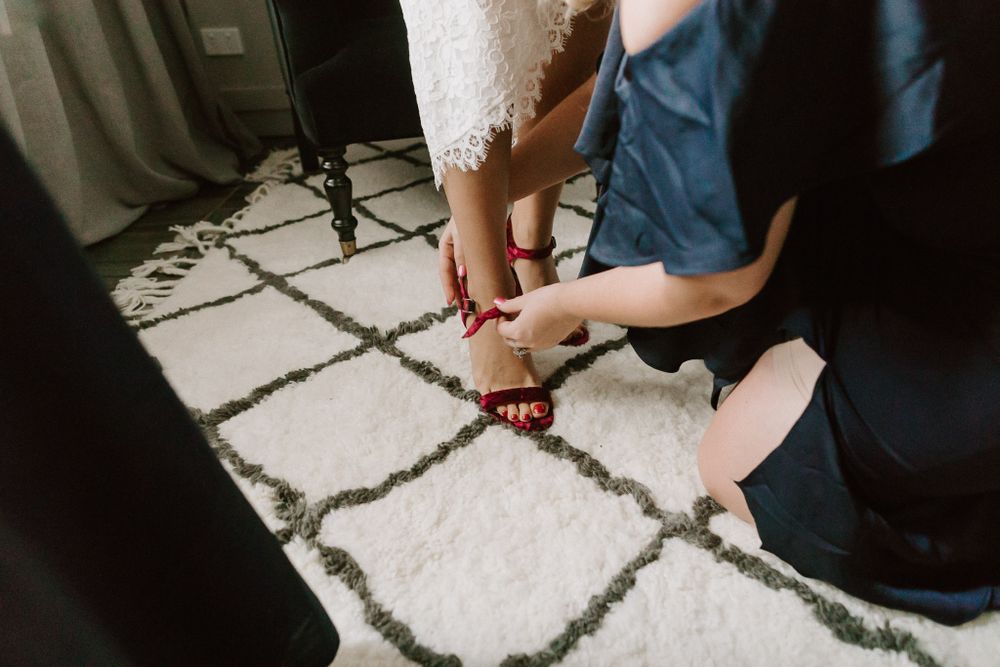 Person helping with wedding shoe fitting on a patterned carpet.