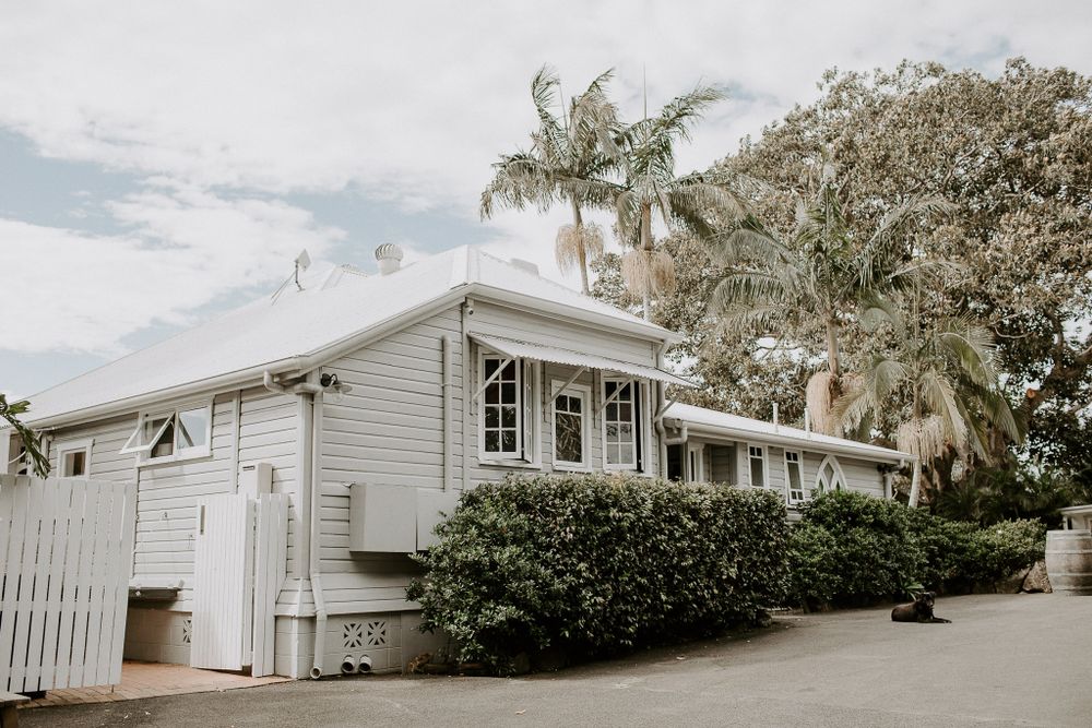 White weatherboard house with colonial style features and palm trees.
