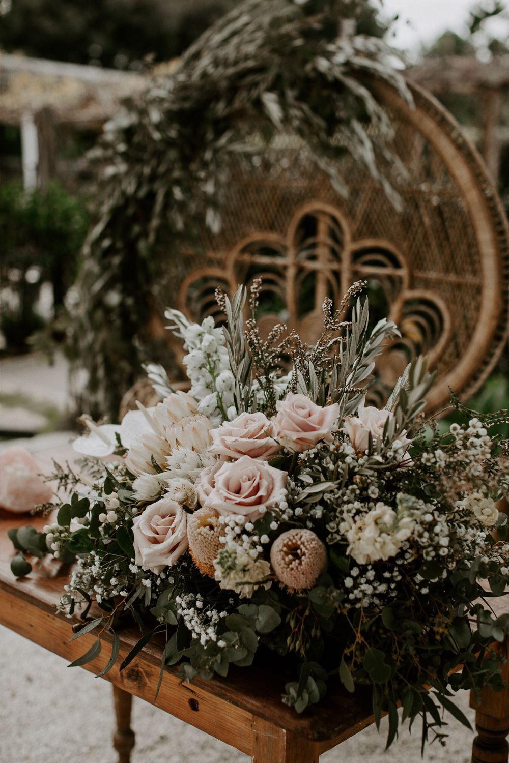 Bohemian wedding floral arrangement with pink roses and white flowers on a peacock chair.