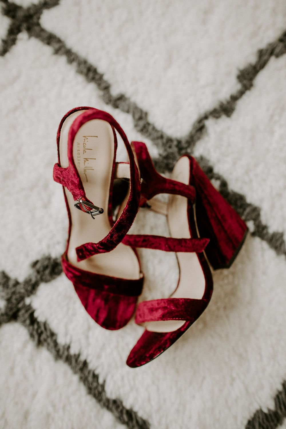 Burgundy velvet wedding shoes on a geometric patterned rug.