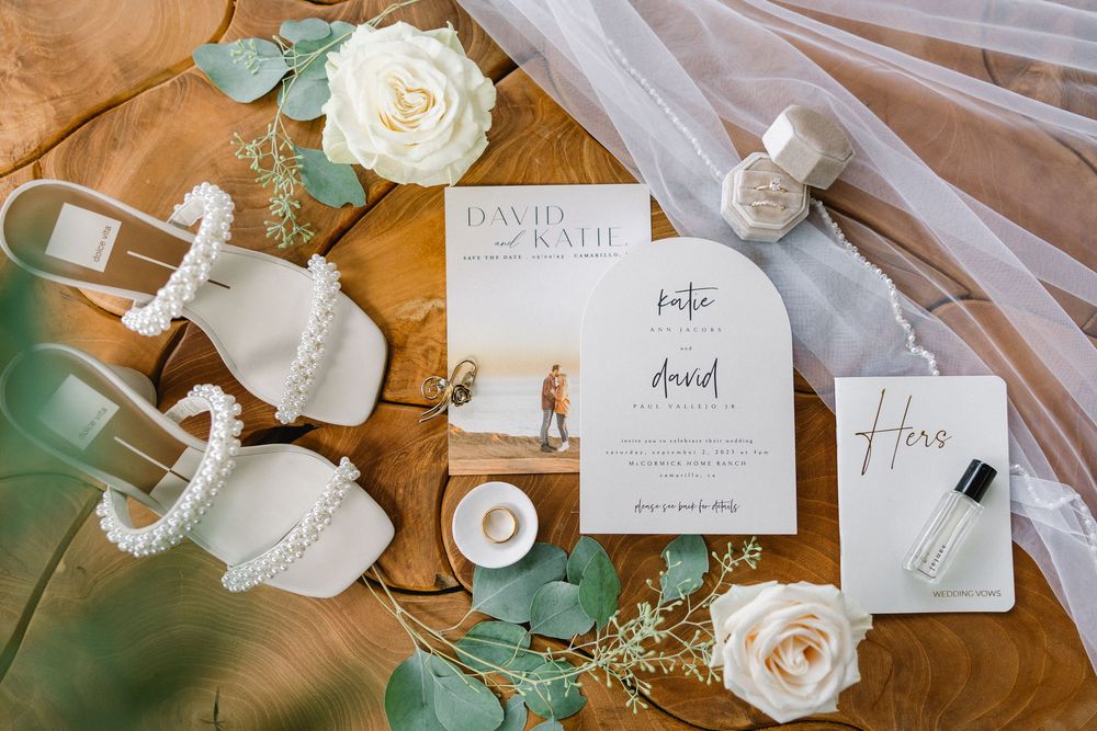 Wedding details flatlay with white roses, invitation cards, bridal shoes and accessories.