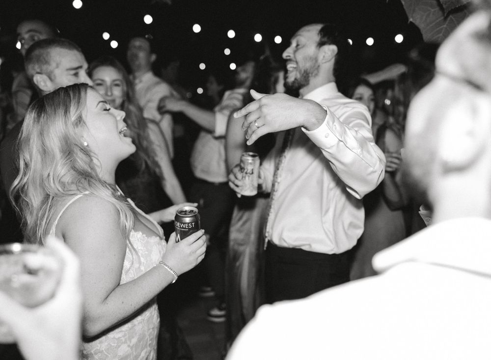 Black and white photo of people dancing and laughing at a party with string lights overhead.