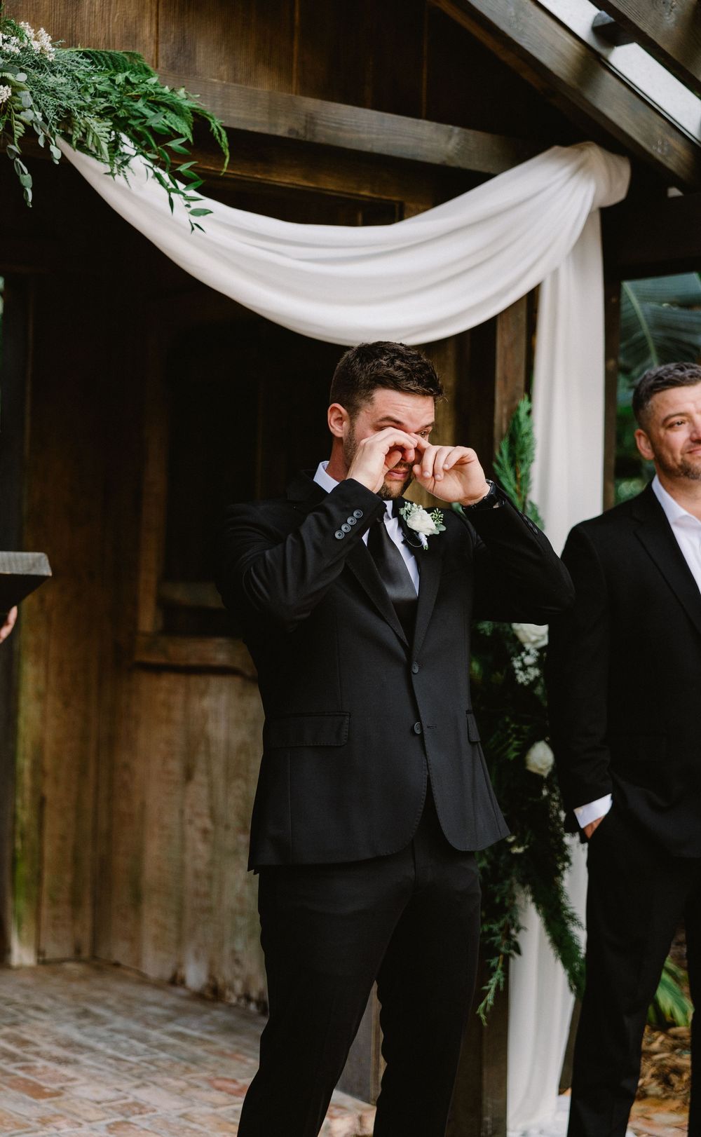 Emotional moment during outdoor wedding ceremony under draped white fabric arch.