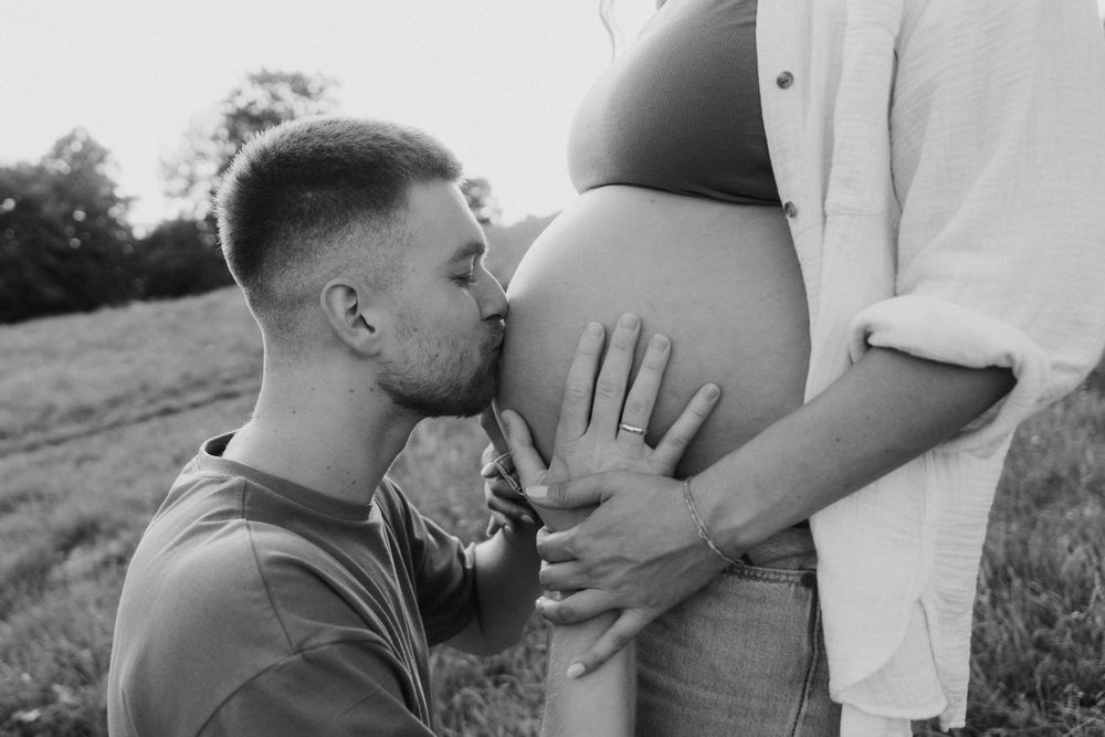 Black and white maternity photography sequence shows couple sharing intimate moments in an outdoor field setting.