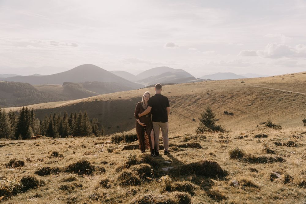 Couple standing on a rock embracing while overlooking scenic mountain landscape with rolling hills.