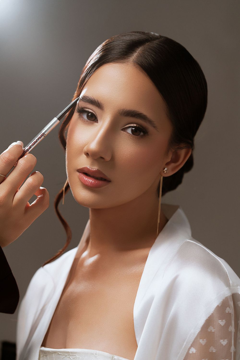 Professional makeup artist applying cosmetics to model wearing white robe in studio with dramatic lighting.