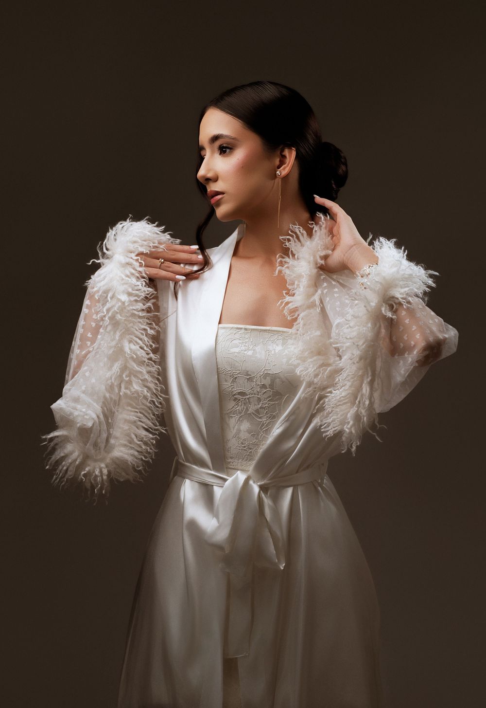 A dramatic fashion portrait series showing a white feathered bridal robe against a dark moody background.